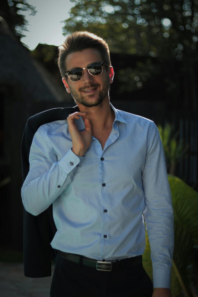 Confident young man in sunglasses poses outdoors in casual attire, exuding style and charisma.